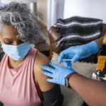 A Black nurse gives a COVID-19 vaccine to a senior Black woman.