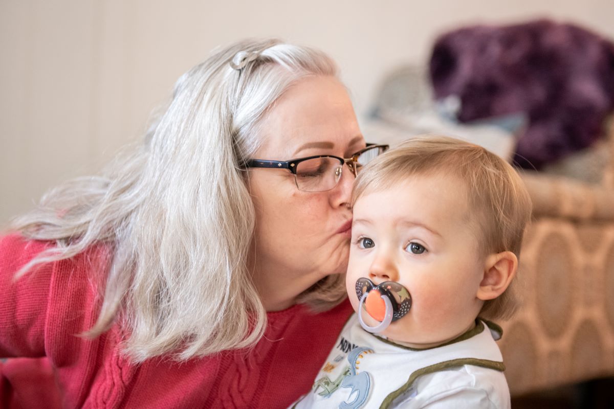 Woman leans over and kisses her infant grandson.