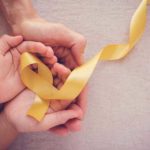Image result of adult and child hands holding a yellow ribbon to represent childhood cancer awareness.