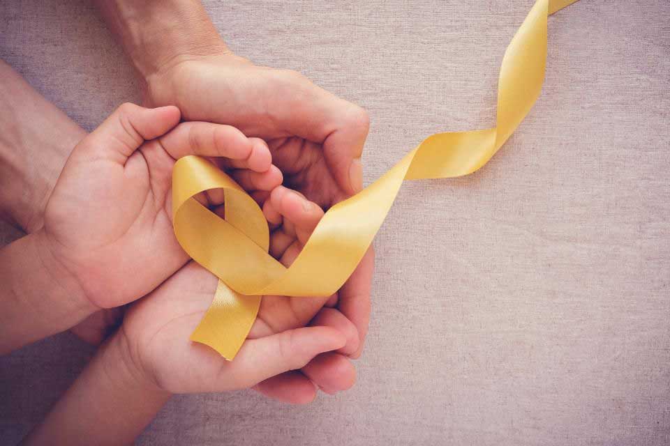 Image result of adult and child hands holding a yellow ribbon to represent childhood cancer awareness.