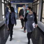 Four people – two women followed by two men – walk down a hallway with signage that reads “Penn State College of Medicine” and “Institute for Personalized Medicine.” As they walk, they look to their right, out of a set of windows.