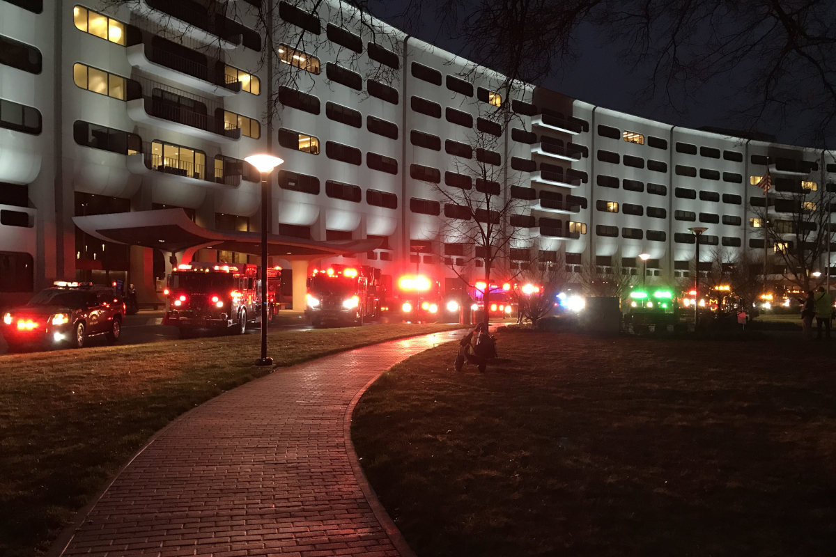Several emergency vehicles and tow trucks with flashing lights park along the crescent at Hershey Medical Center, at dusk.