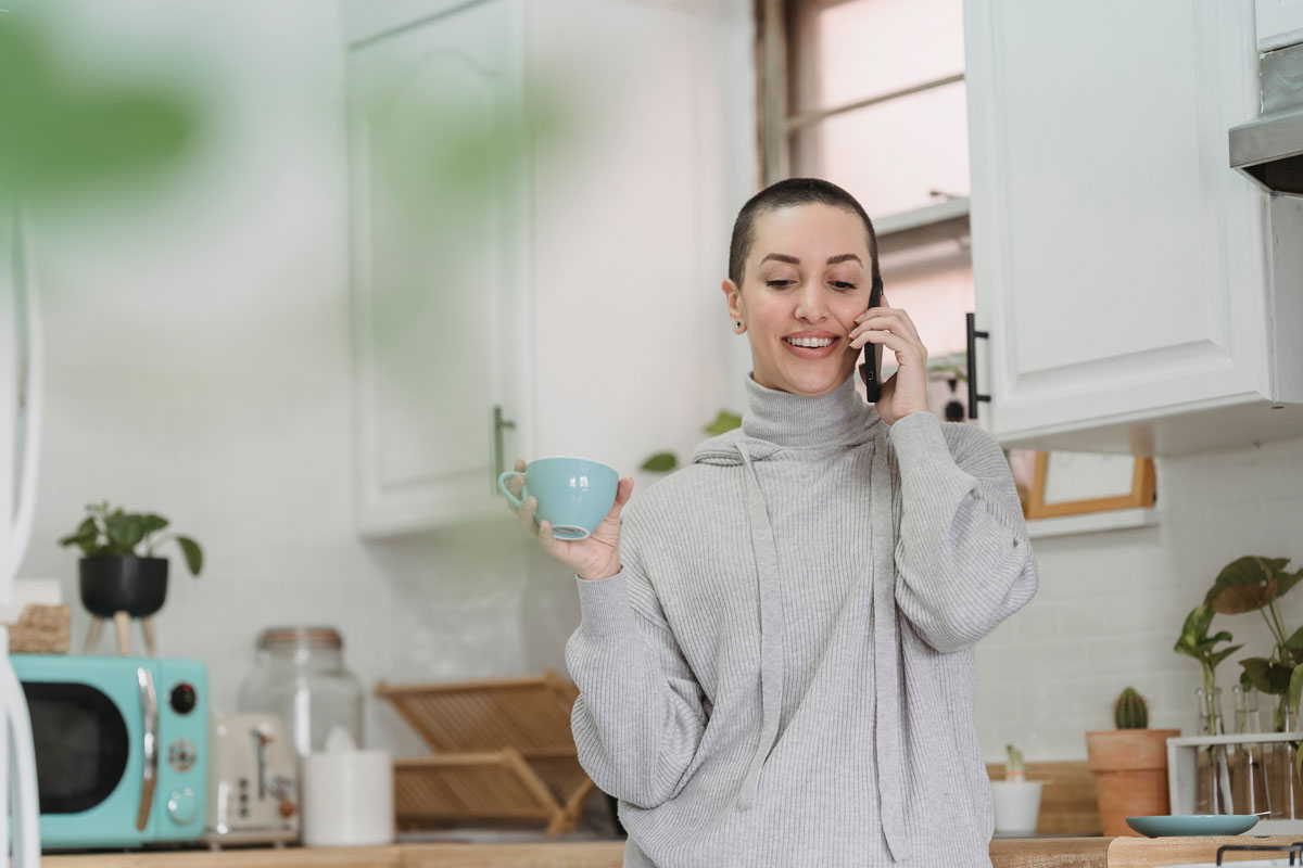Cheerful woman talking on smartphone in kitchen