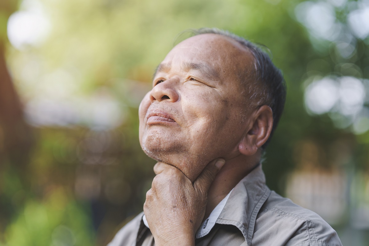 An elderly man holds his sore throat.