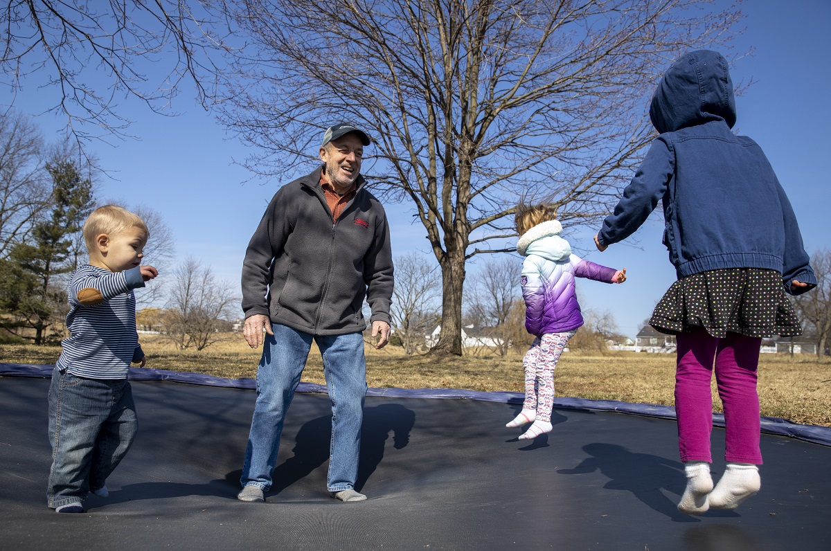 Man jumps on trampoline with three young grandchildren.