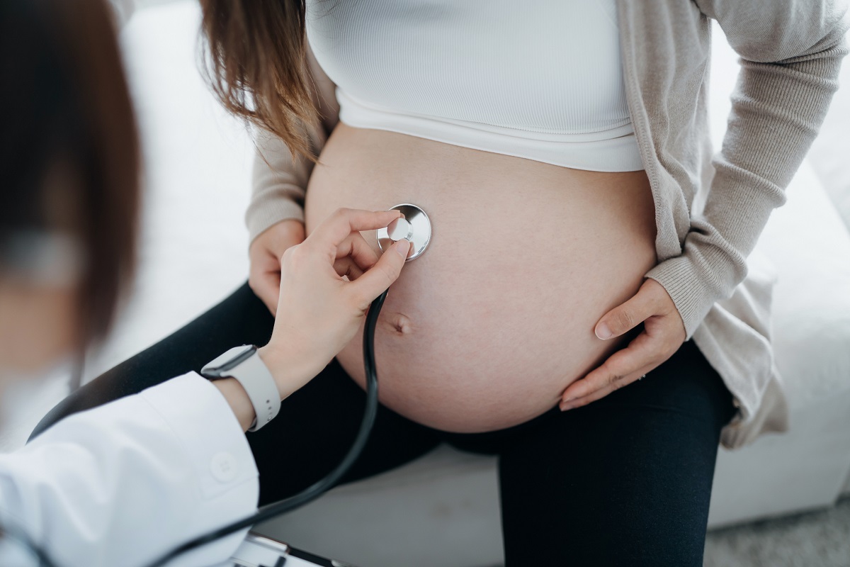 Close up of a health care provider doing checkup on a pregnant woman, examining the belly with stethoscope.