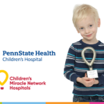 A young boy holds a small trophy. To his left are the logos for Penn State Health Children's Hospital and Children's Miracle Network Hospitals.