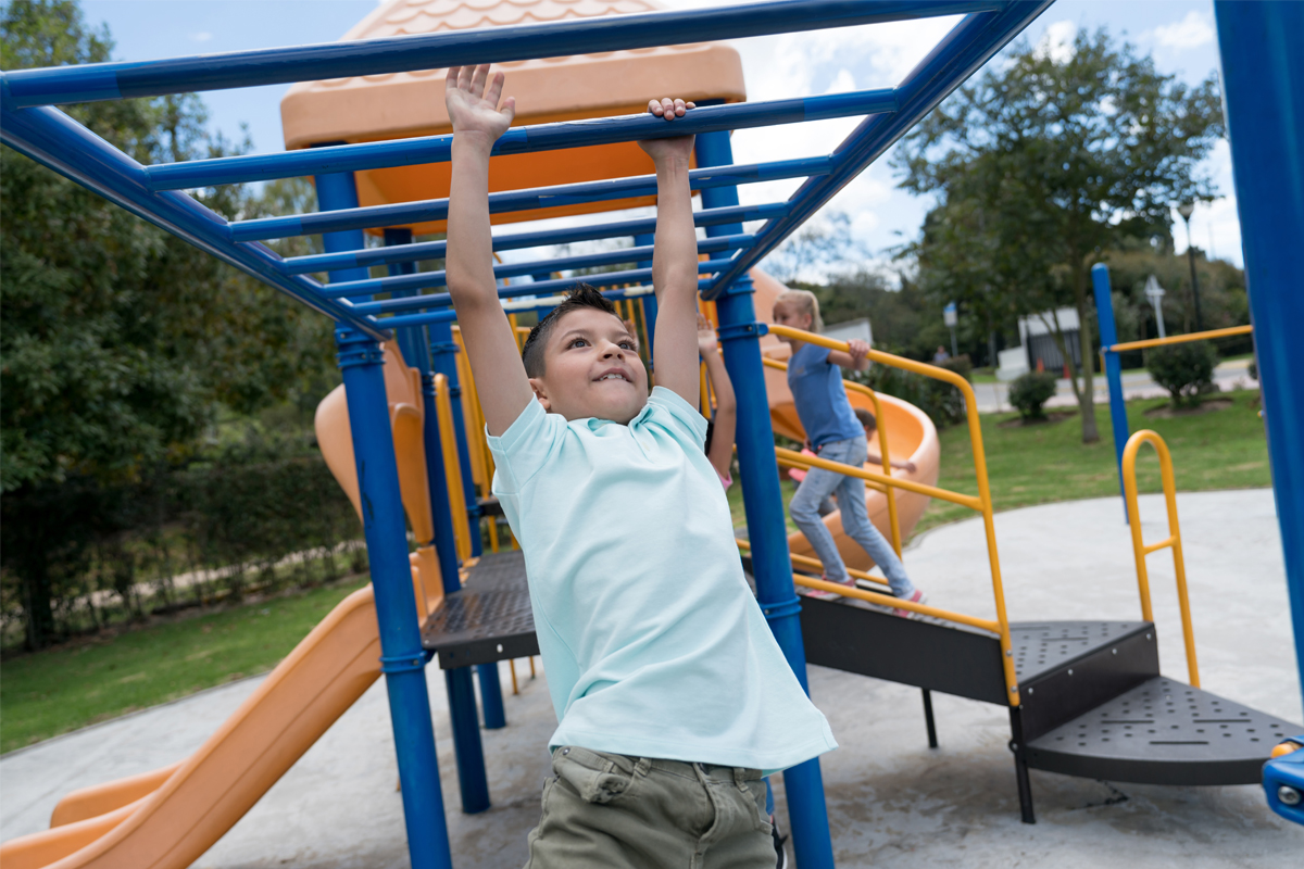 A young girl hangs from playground equipment.