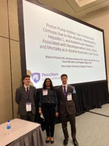 Blaine Prichard, left, Dr. Meghali Nighot and Nathan Morris take a group photo in front of a projector screen at Digestive Disease Week. 