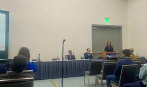 Dr. Lauren Kaminsky stands at a podium in a conference room, with several other people seated in rows of chairs in the foreground, to present a research study during the Digestive Disease Week conference.