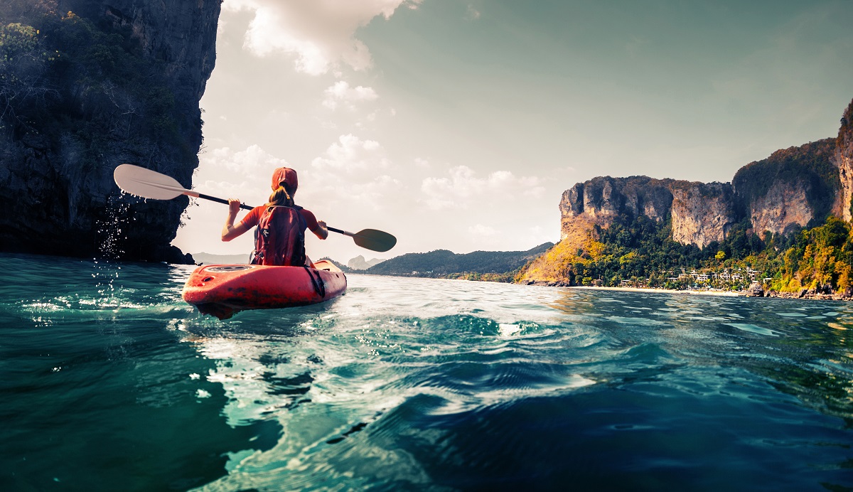 A woman paddles a kayak in a calm, tropical bay.