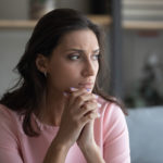 Worried young indian Arabic woman sit on couch at home look in distance thinking pondering, anxious unhappy arab mixed race female suffer from mental psychological personal problems, mourn or yearn.