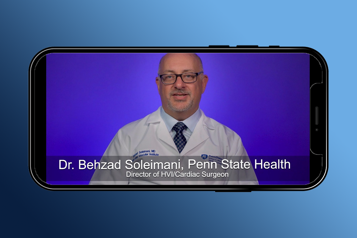 Dr. Bahzad Soleimani, Heart and Vascular Institute director and cardiac surgeon, talks during a video on a cell phone. He is wearing a white coat with his name and Penn State Heart and Vascular Institute on the left and the Hershey Medical Center logo on the right. A graphic identifies him as Dr. Bahzad Soleimani, Penn State Health, Director of HVI/Cardiac Surgeon.