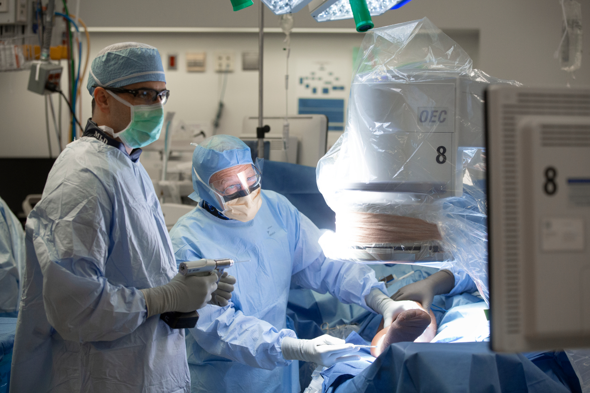 Two doctors in personal protective equipment stand next to an operating table with a patient on it.