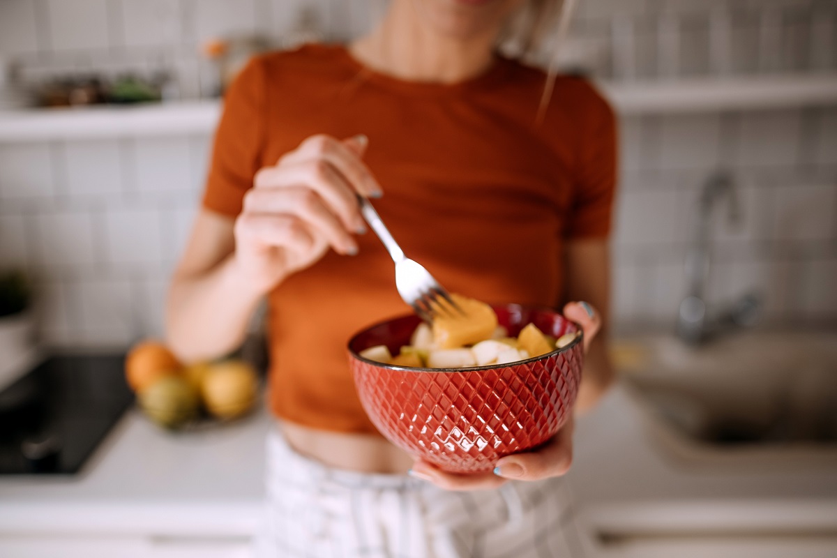 Young woman eating fruit salad in the kitchen