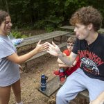 A girl and a boy smile at one another as they attempt a handshake.