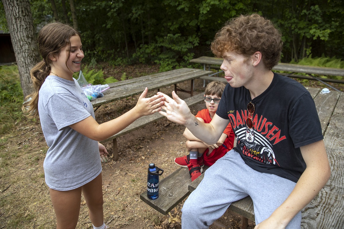 A girl and a boy smile at one another as they attempt a handshake.