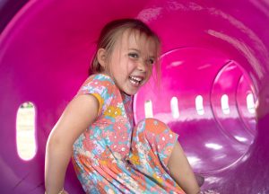 A little girl laughs inside a plastic tube at a playground.
