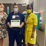 Nurse posing with a certificate, two women – one posing on either side of the nurse