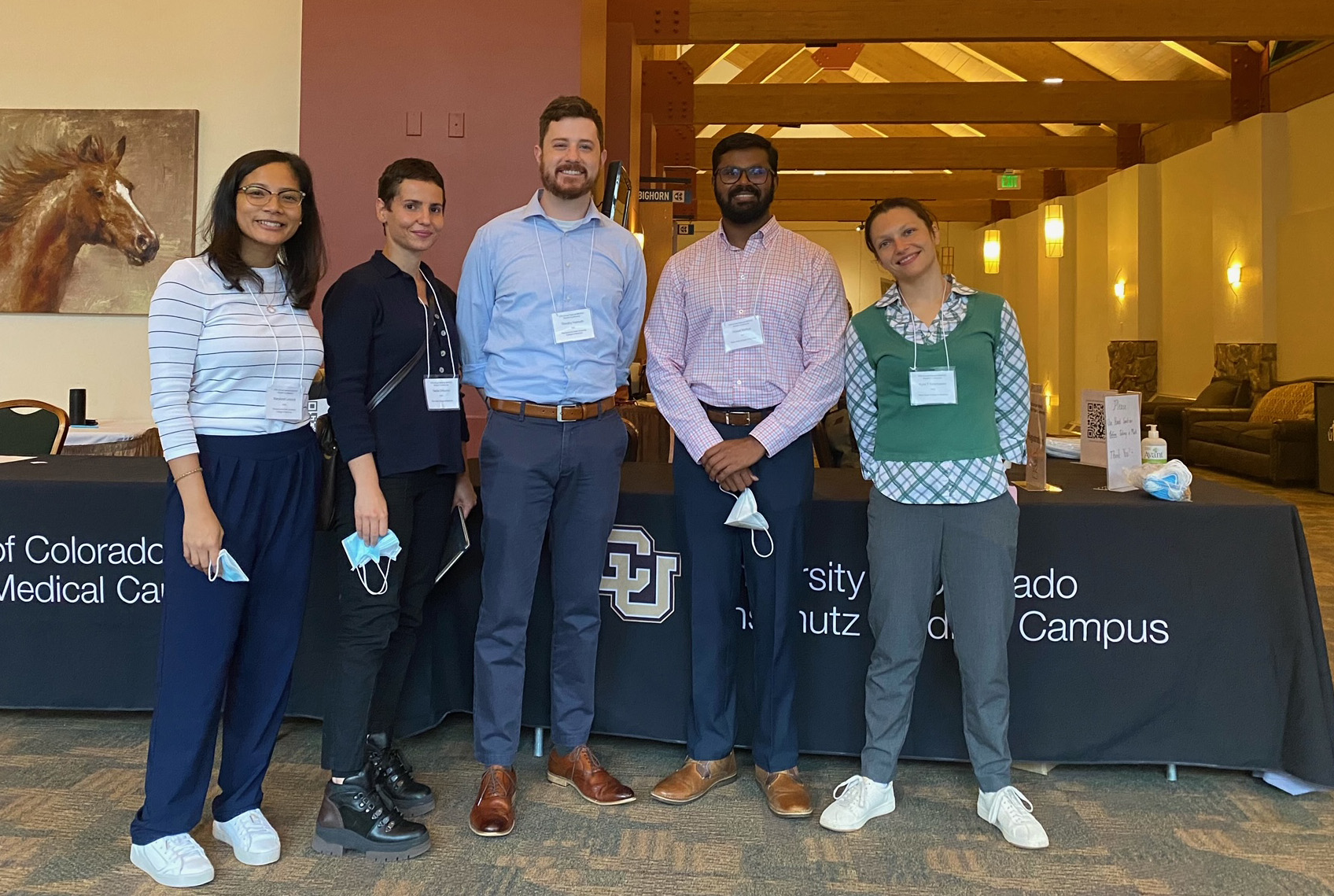 MD/PhD students Maryknoll Linscott, Nadia DiNunno, Tim Helmuth, Havell Markus and Kyra Newmaster pose in a line for a photo inside a conference building.