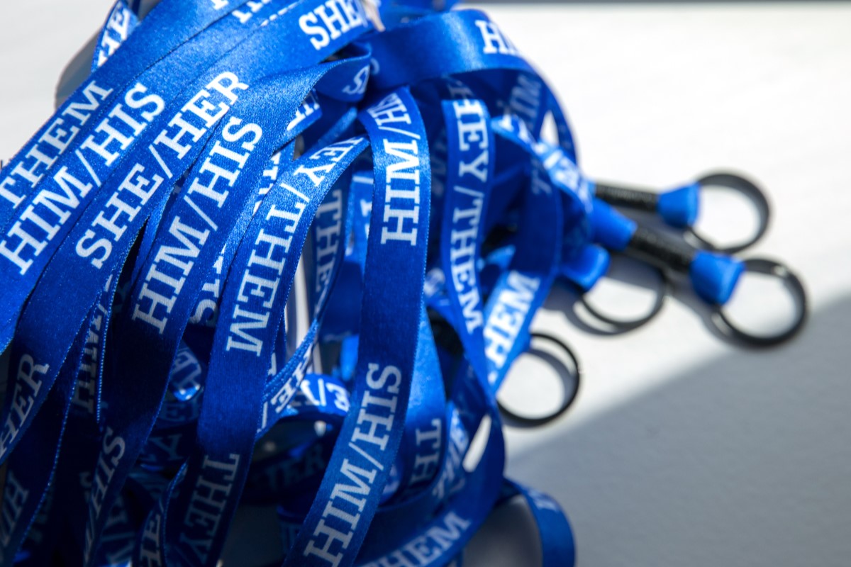Pile of blue lanyards, each with the words “she/her,” “him/his” or “they/them”