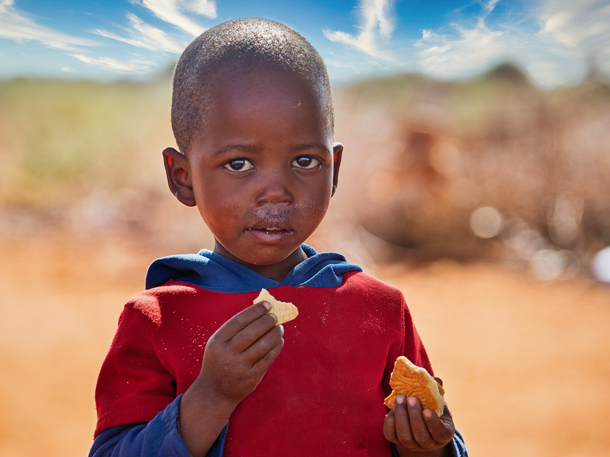 A young boy in Africa eats a small piece of a biscuit.