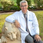 Dr. David Rabago sits by a statue of the nittany lion on Penn State College of Medicine's campus.