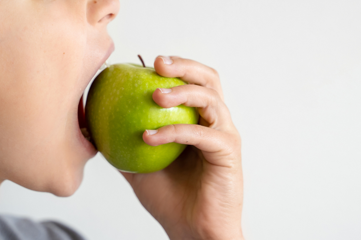 A close-up of a child biting into a green apple.