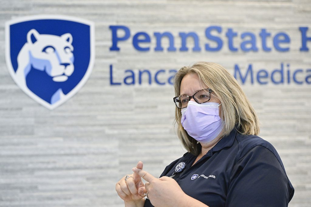 A woman with a face mask is gesturing instructions as the main greeter for the hospital.