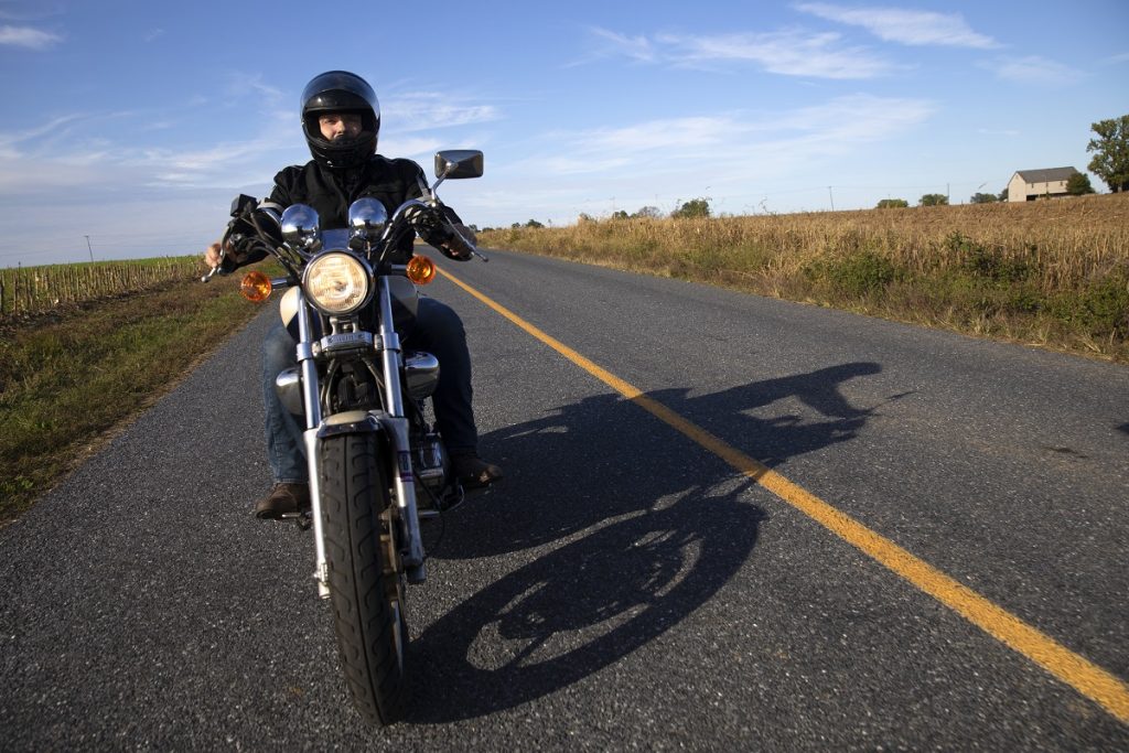 A man in leather and a helmet rides a motorcycle down a highway painted with a double yellow line.