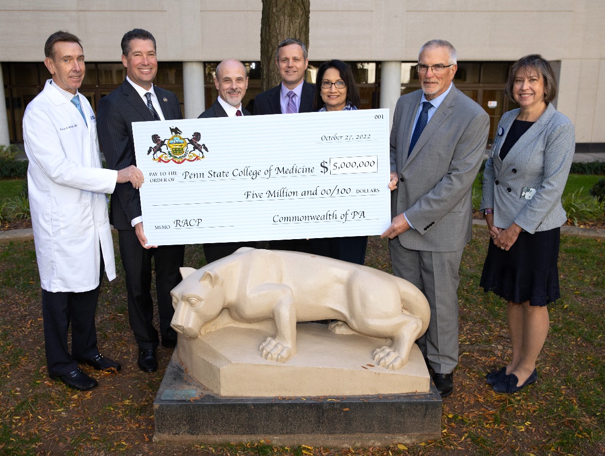 Dr. Kevin Black, interim dean for Penn State College of Medicine; State Representative Tom Mehaffie; Jake Smeltz, chief of staff for the office of Speaker Bryan Cutler, PA House of Representatives; Chuck Erdman, chief of staff for State Senator John DiSanto; Neeli Bendapudi, president of Penn State; Ronald Wilson, chair for the Department of Comparative Medicine and Dr. Leslie Parent, vice dean of research and graduate studies pose for a photo behind the Nittany Lion statue at Penn State College of Medicine. They are holding a commemorative check for $5 million dollars.