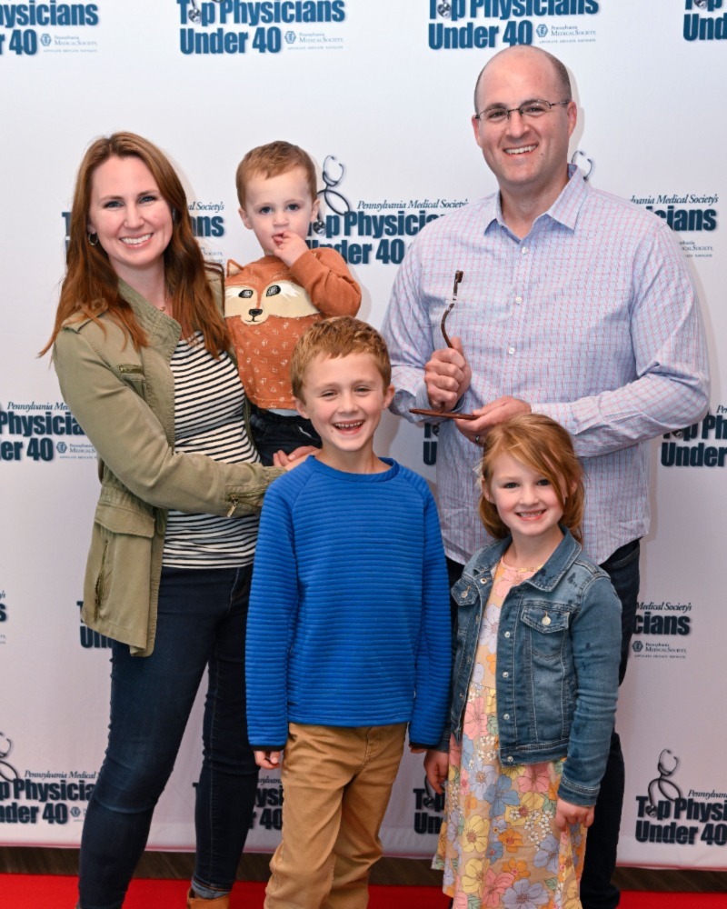 Dr. Kevin Rakszawski, right, stands for a group photo with his wife Elizabeth, left, surrounded by their three young children.