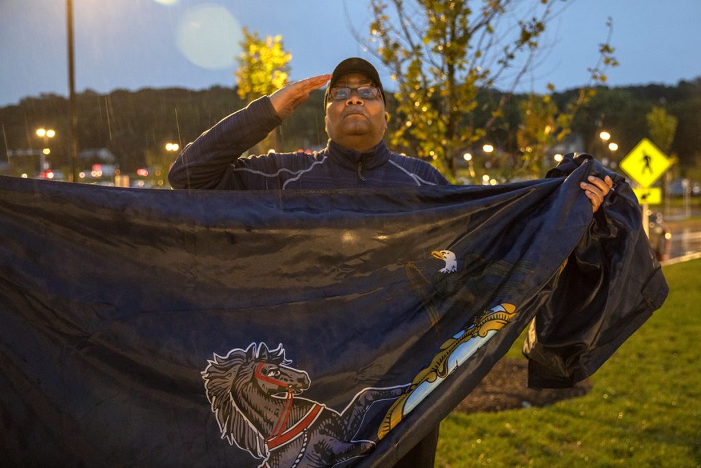 A man holds a dark looking flag while saluting.