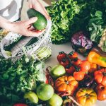 Young woman returned with purchases from grocery store takes fresh organic vegetables out of mesh bag putting on kitchen table at home close view
