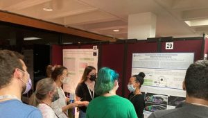 Rachelle Saint-Fort explains her research to six other people, who are gathered around her poster. 