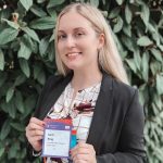 Carli King stands outdoors and holds the nametag badge she wore while attending the World Cancer Congress in Geneva, Switzerland.