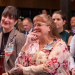Two women sitting in an audience smiling.