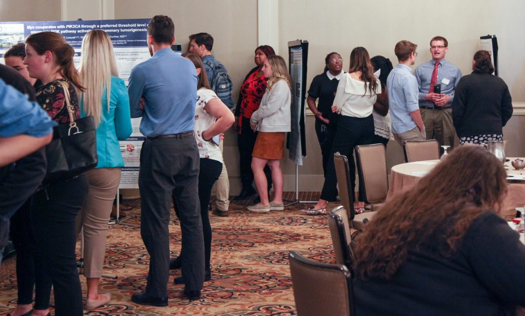 Fall retreat attendees talk or line up in various groups in a hotel ballroom to look at poster presentations.