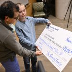 A young boy holds an oversized check, presenting it to a man in surgical scrubs.