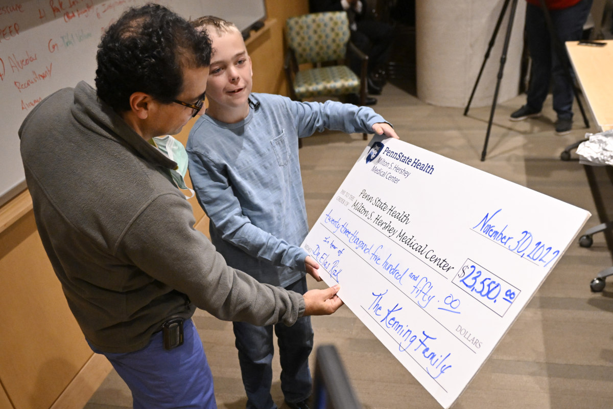 A young boy holds an oversized check, presenting it to a man in surgical scrubs.