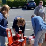People in masks and wearing Penn State Health gear go through boxes in a parking lot.