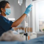Hospital Ward: Professional head nurse wearing face mask does checkup of patient's vitals, checking heart rate computer.