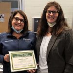 Two women smile at the camera. One holds a plaque.