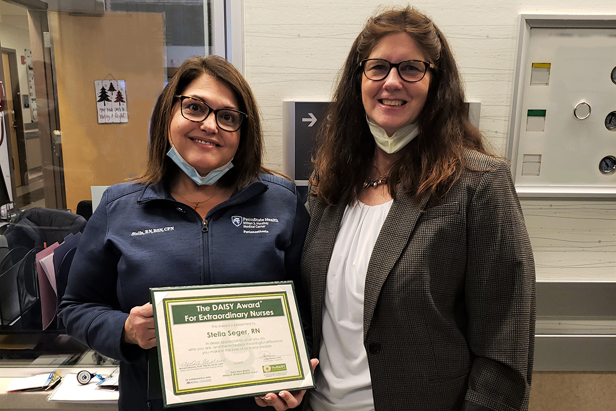 Two women smile at the camera. One holds a plaque.