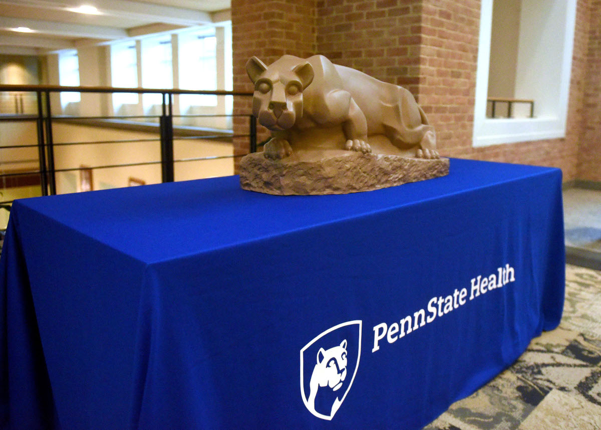 A lion statue sits on top of a table. The table has a logo on it that says, 