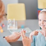Adorable smiling little caucasian girl standing and using sign language to communicate with child psychologist in a clinic. Mental health professional teaching deaf kid to speak through hand gestures.