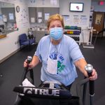 A woman wearing a mask exercises on an elliptical.