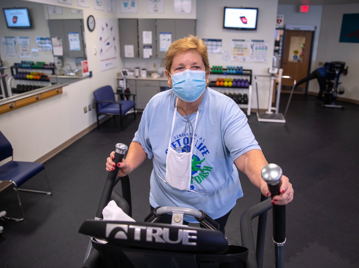 A woman wearing a mask exercises on an elliptical.