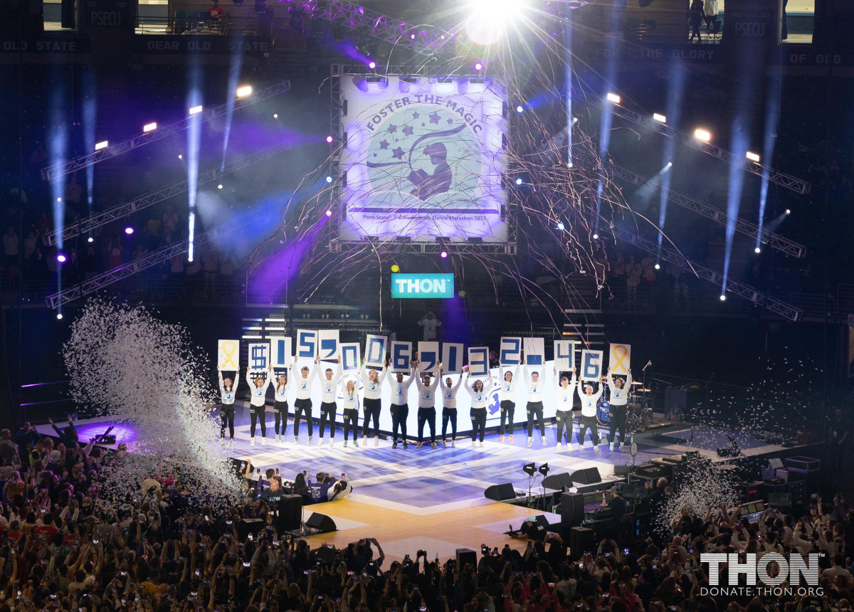 Several individuals stand on a stage at Bryce Jordan Center holding up individual signs spelling out the amount $15,006,132.46.