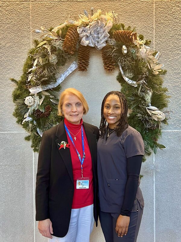 Mary Beth Miele, PhD, director of the Medical Laboratory Science Program at Penn State College of Medicine, stands beside Tytiana Taylor, a student in the program. They are standing against a wall where a holiday wreath is hanging.